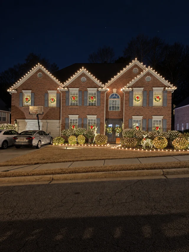 Roofline lighting with window wreaths and illuminated shrubs.