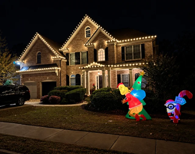 Warm white roofline lighting on a brick home with holiday yard decorations.