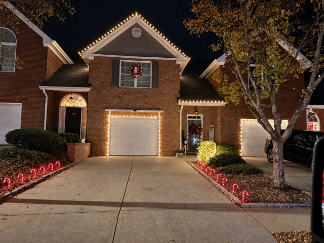Warm white lights outlining a garage and gable, with red candy cane lights along the driveway.