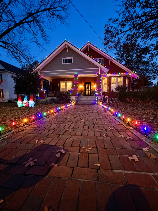Multicolor lighting along a brick walkway, porch columns, and roofline.