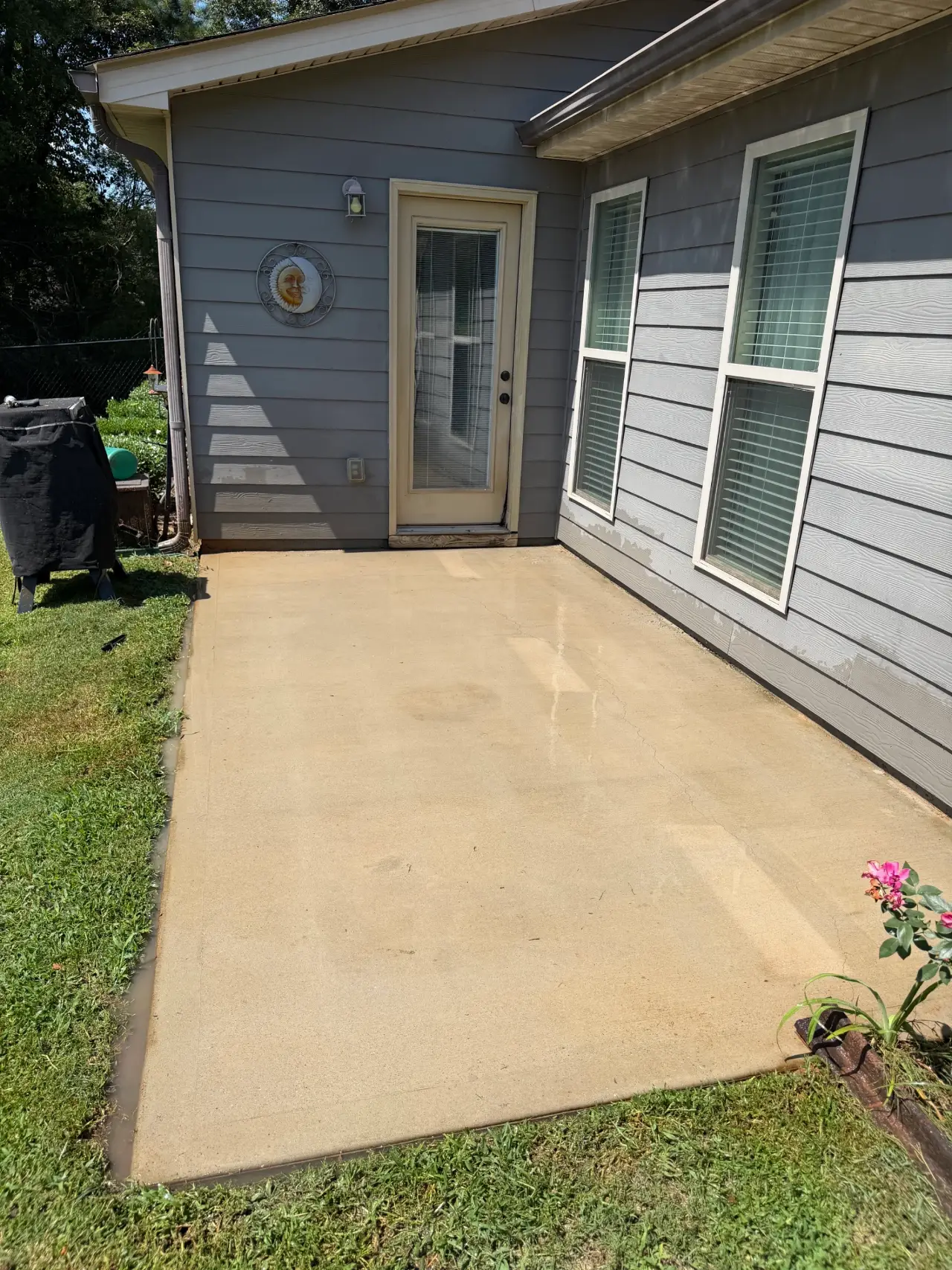 Clean concrete patio beside a gray house after pressure washing
