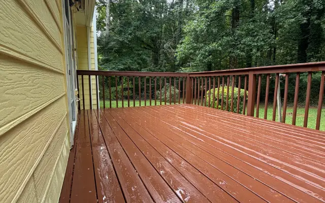 After photo of a wet painted wood deck and railing beside a yellow-sided home.
