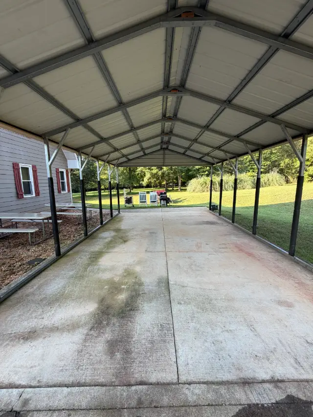 Covered concrete parking area beneath a metal carport beside a home.