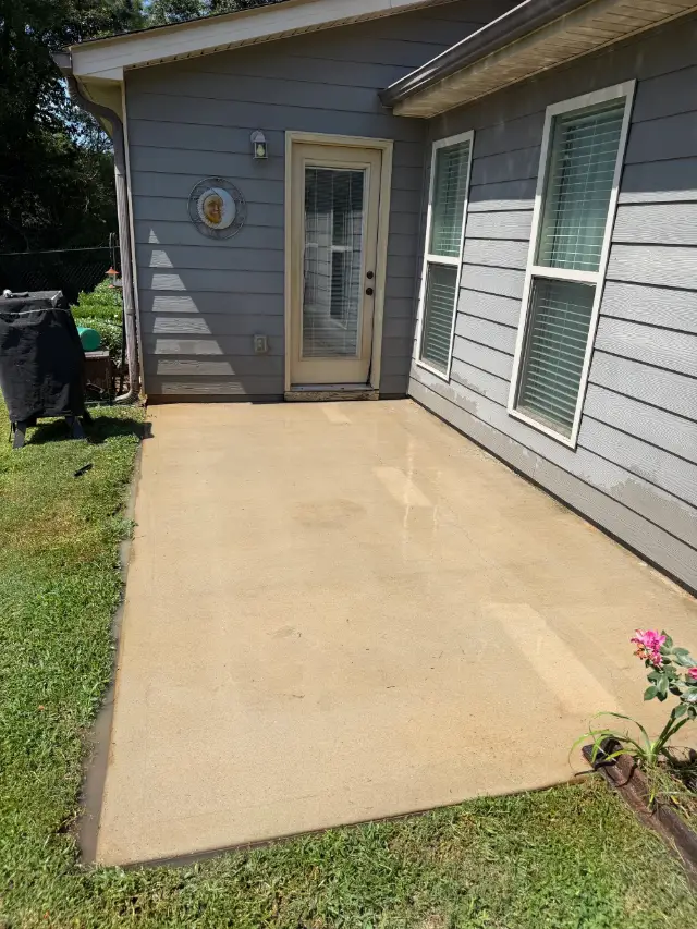 Clean concrete patio beside a gray house after pressure washing