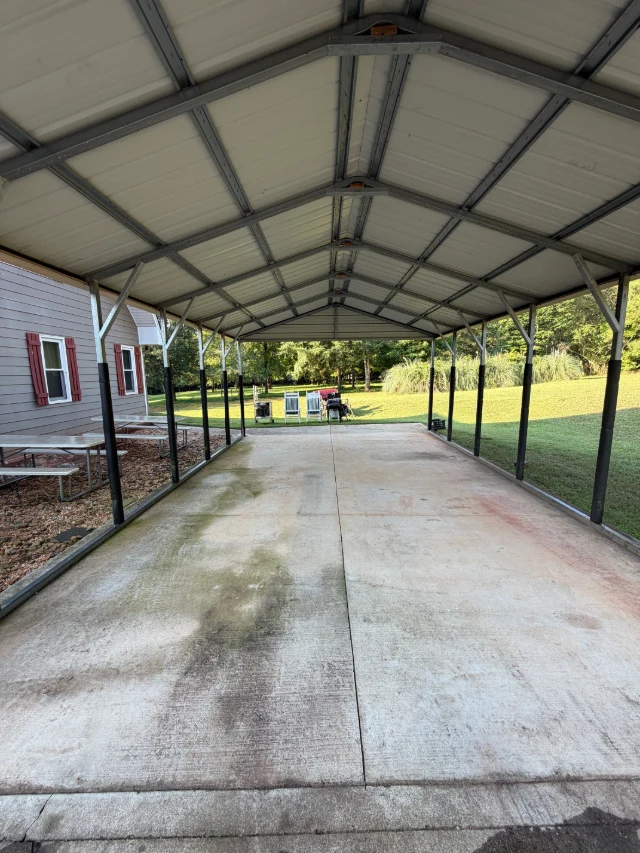 Covered concrete parking area beneath a metal carport beside a home.
