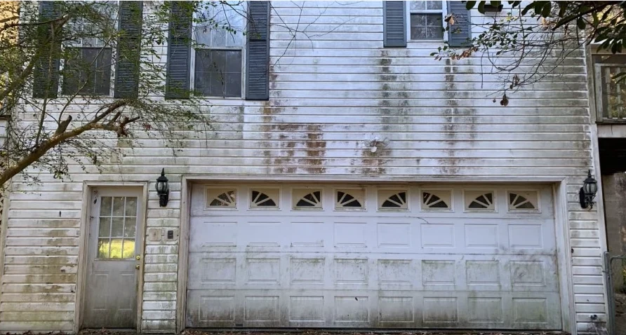 White two-story home and garage before washing with dark algae and dirt streaks on the siding and garage door.