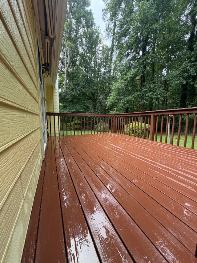 After photo of a wet painted wood deck and railing beside a yellow-sided home.