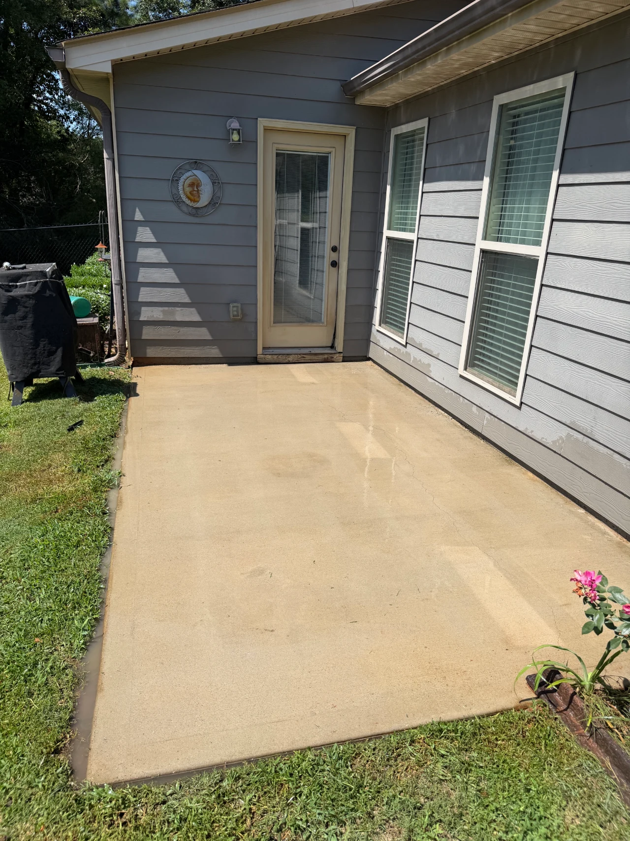 Clean concrete patio beside a gray house after pressure washing